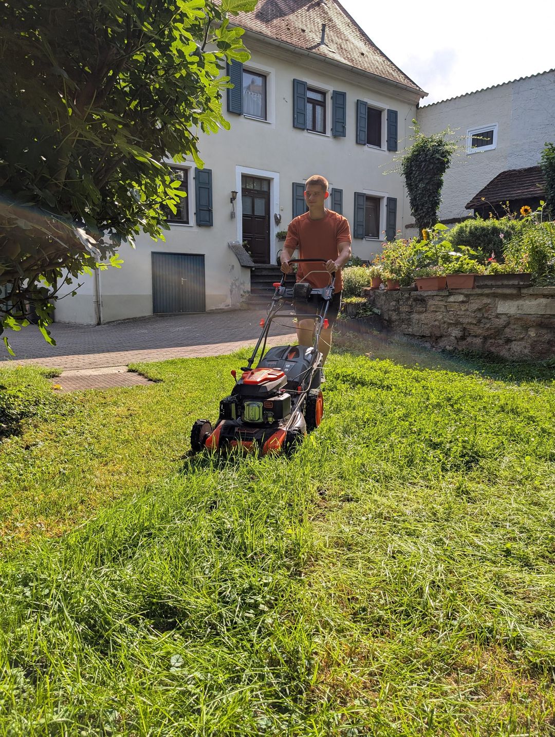 Helfer von SB-Gartenpflege mäht einen Rasen vor einem Wohnhaus in Rheinhessen